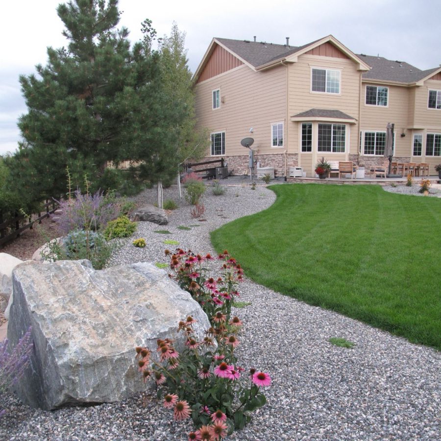 Water-wise rock garden with boulders and flowering plants next to a lawn
